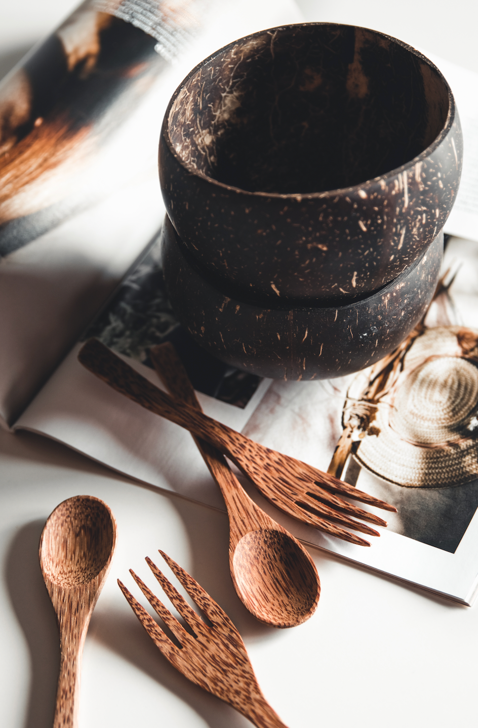Earth Cutlery Collection handcrafted coconut wood spoons and forks arranged around two natural coconut bowls on an open magazine, eco-friendly sustainable cutlery set by Koko Loko