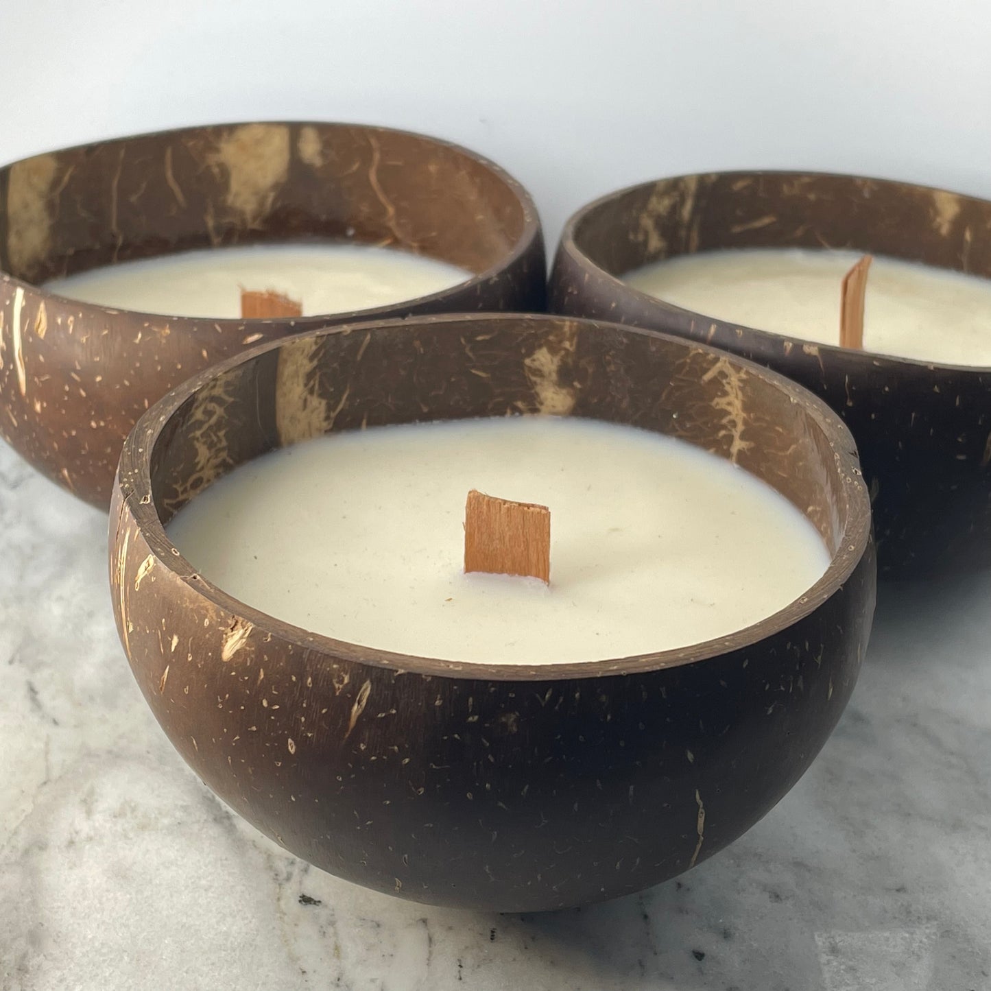 Koko Loko Tropical Candle Collection set of three handcrafted coconut wax candles in natural coconut shell bowls with wooden wicks arranged in a triangle on a marble surface, eco-friendly candle gift set by Koko Loko