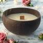 Refreshing Rose Candle in a natural coconut shell bowl with a wooden wick on a marble surface surrounded by fresh pink and white roses, handcrafted coconut wax candle by Koko Loko

