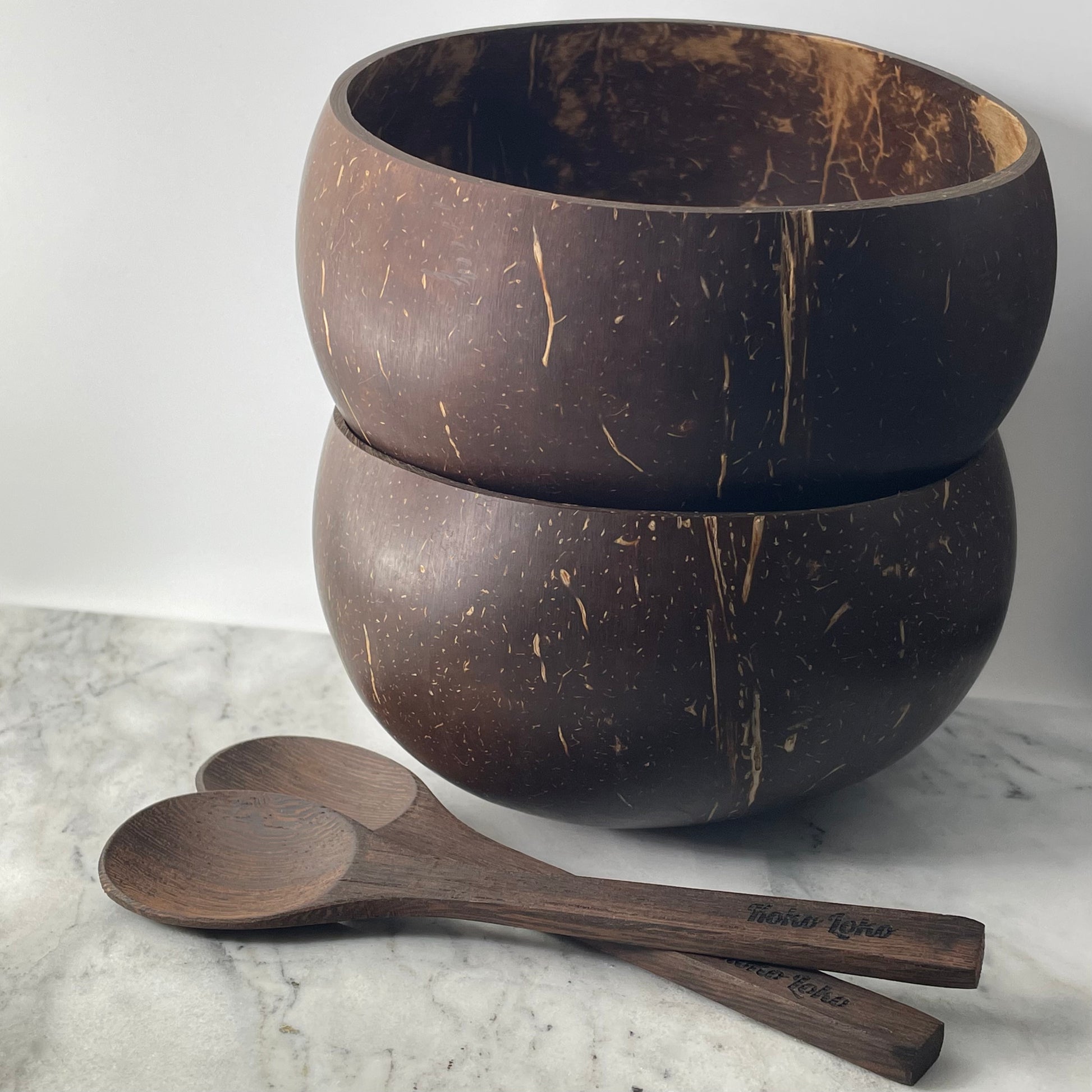 Koko Loko Combo set featuring two natural coconut shell bowls stacked on a marble surface with two handcrafted ebony wood spoons with Koko Loko engraving in front, eco-friendly gift set by Koko Loko
