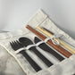 Nirvana Cutlery Collection ebony wood fork, spoon and knife with dark wood chopsticks, bamboo straw and cleaner brush laid out in an open white cotton roll pouch with Koko Loko engraving on a marble surface, eco-friendly sustainable cutlery set by Koko Loko

