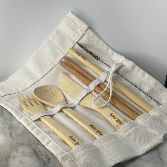 Panda Cutlery Collection bamboo fork, spoon, knife, chopsticks and straw with cleaner brush laid out in an open white cotton roll pouch with Koko Loko engraving on a marble surface, eco-friendly sustainable cutlery set by Koko Loko
