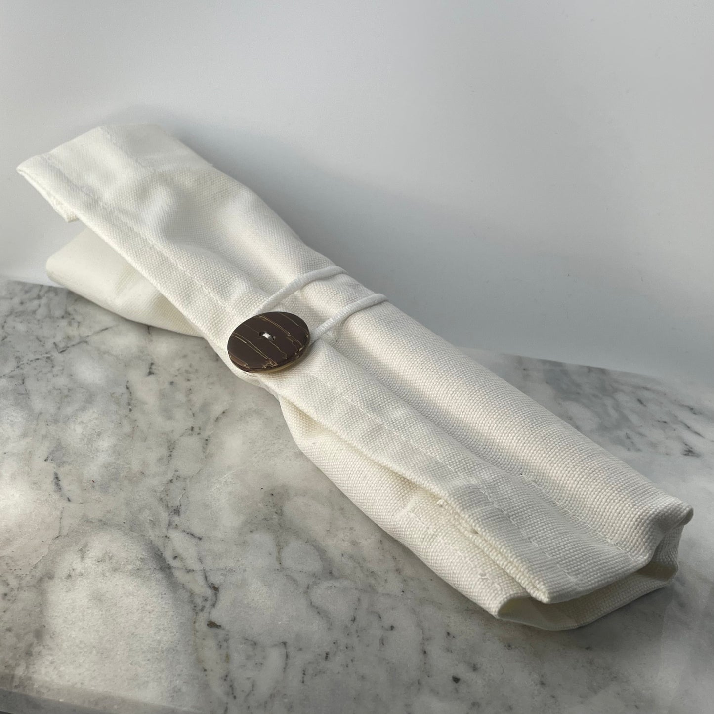 Earth Cutlery Collection white cotton roll pouch tied closed with a coconut shell button on a marble surface, eco-friendly travel cutlery storage by Koko Loko
