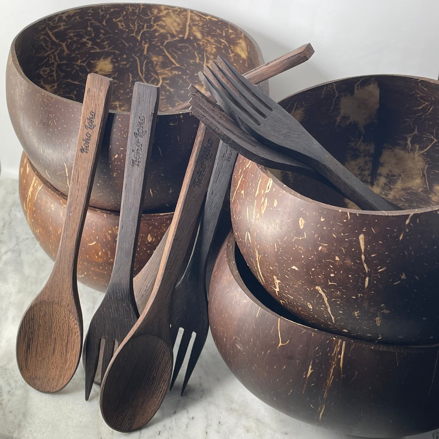 Koko Loko Family Collection featuring four natural coconut shell bowls stacked in two pairs with four handcrafted ebony wood spoons and forks with Koko Loko engraving arranged in front on a marble surface, eco-friendly sustainable gift set by Koko Loko
