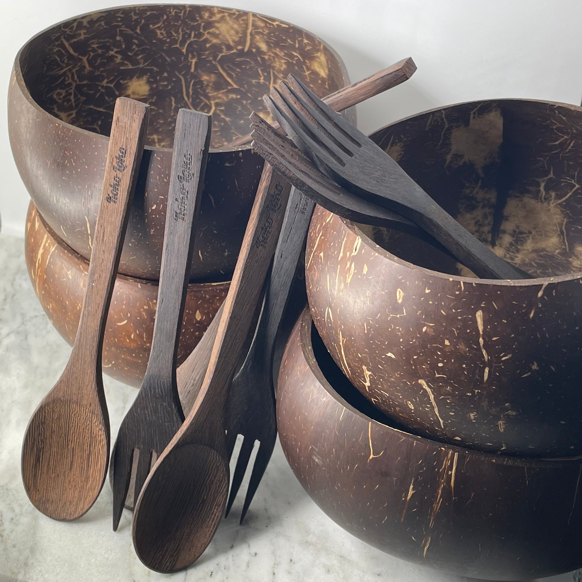 Koko Loko Family Collection featuring four natural coconut shell bowls stacked in two pairs with four handcrafted ebony wood spoons and forks with Koko Loko engraving arranged in front on a marble surface, eco-friendly sustainable gift set by Koko Loko
