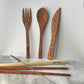 Earth Cutlery Collection handcrafted coconut wood fork, spoon and knife with Koko Loko engraving standing upright against a white wall above dark wood chopsticks, bamboo straw and cleaner brush on a marble surface, eco-friendly sustainable cutlery set by Koko Loko
